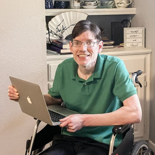 Picture of a man inside with a laptop sitting in a wheelchair